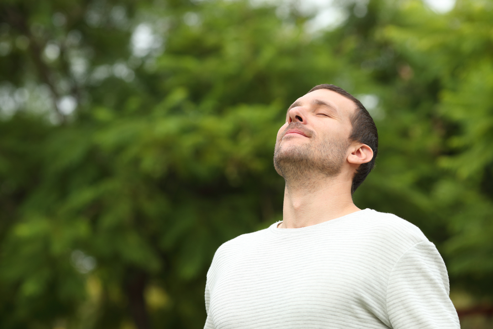 Man takes a deep breath while outdoors in nature.